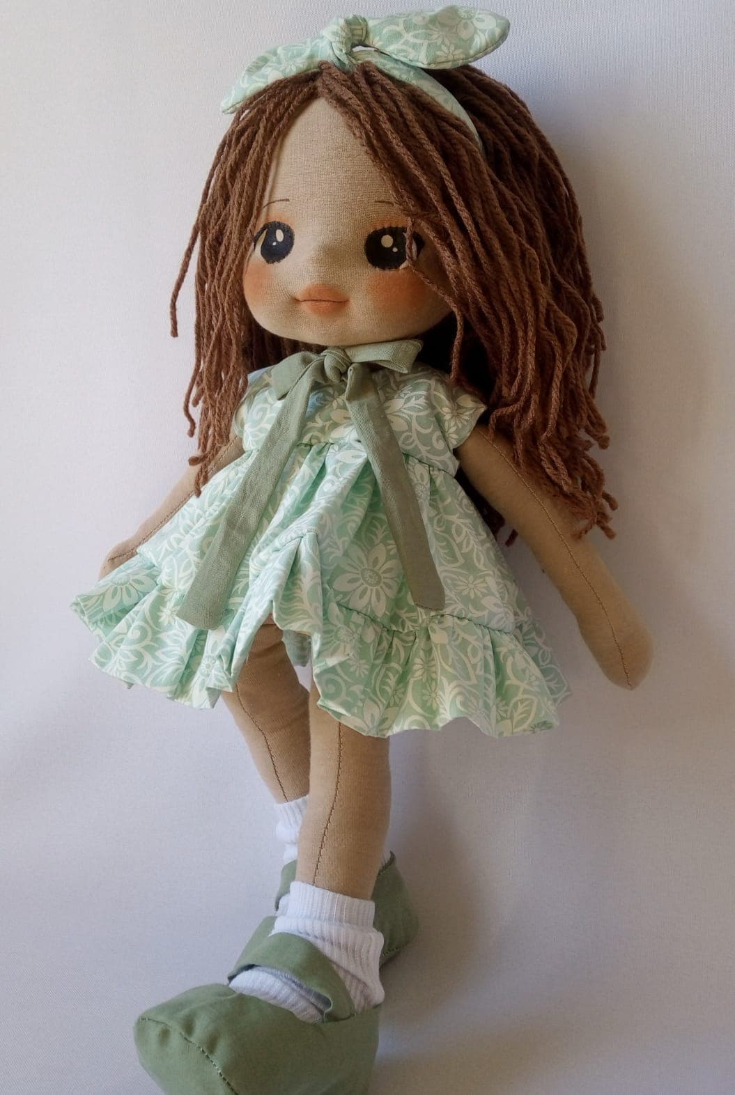 Boneca de pano morena com vestido verde claro, sapatos verde escuro e cabelo castanho.