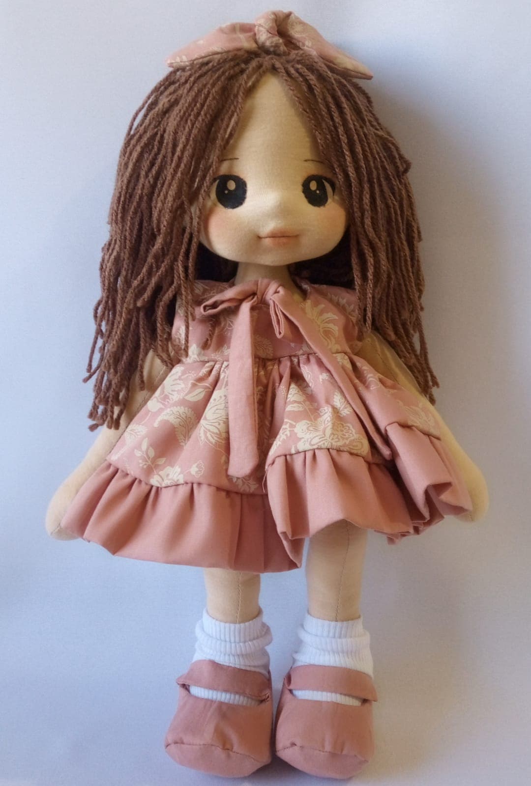 Boneca de pano morena com vestido salmão, desenhos e sapatos salmão, cabelo castanho.