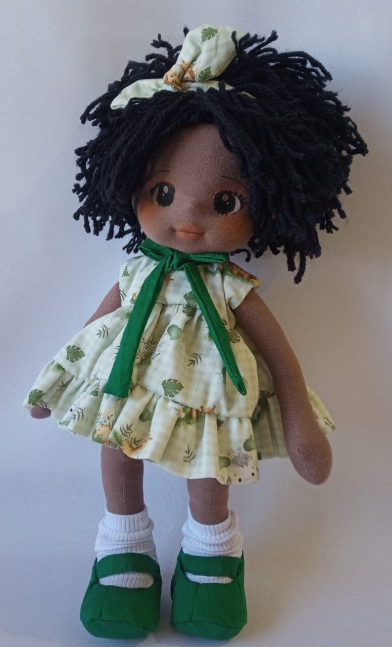Boneca de pano negra com vestido verde, sapatos verde escuro e cabelo preto curto.