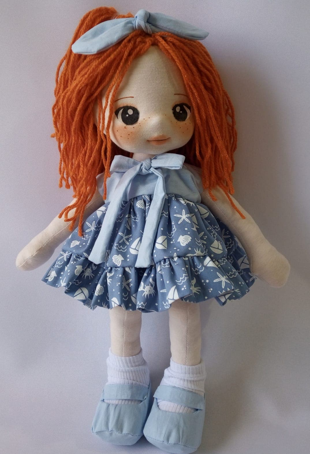 Boneca de pano ruiva com vestido azul, desenho marinho, sapato azul claro e laço azul claro.