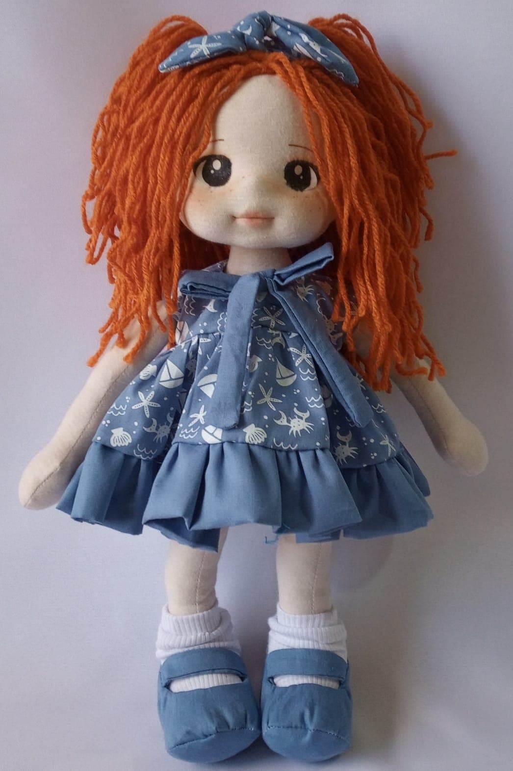 Boneca de pano ruiva com vestido azul, desenho marinho, sapato azul escuro e laço marinho.