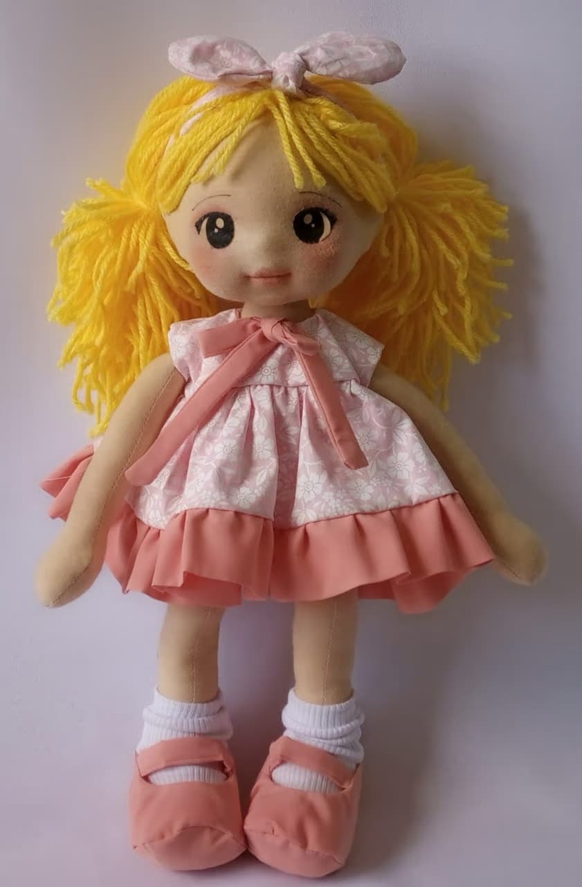 Boneca de pano loira com vestido rosa claro, sapatos rosa escuro e olhos escuros
