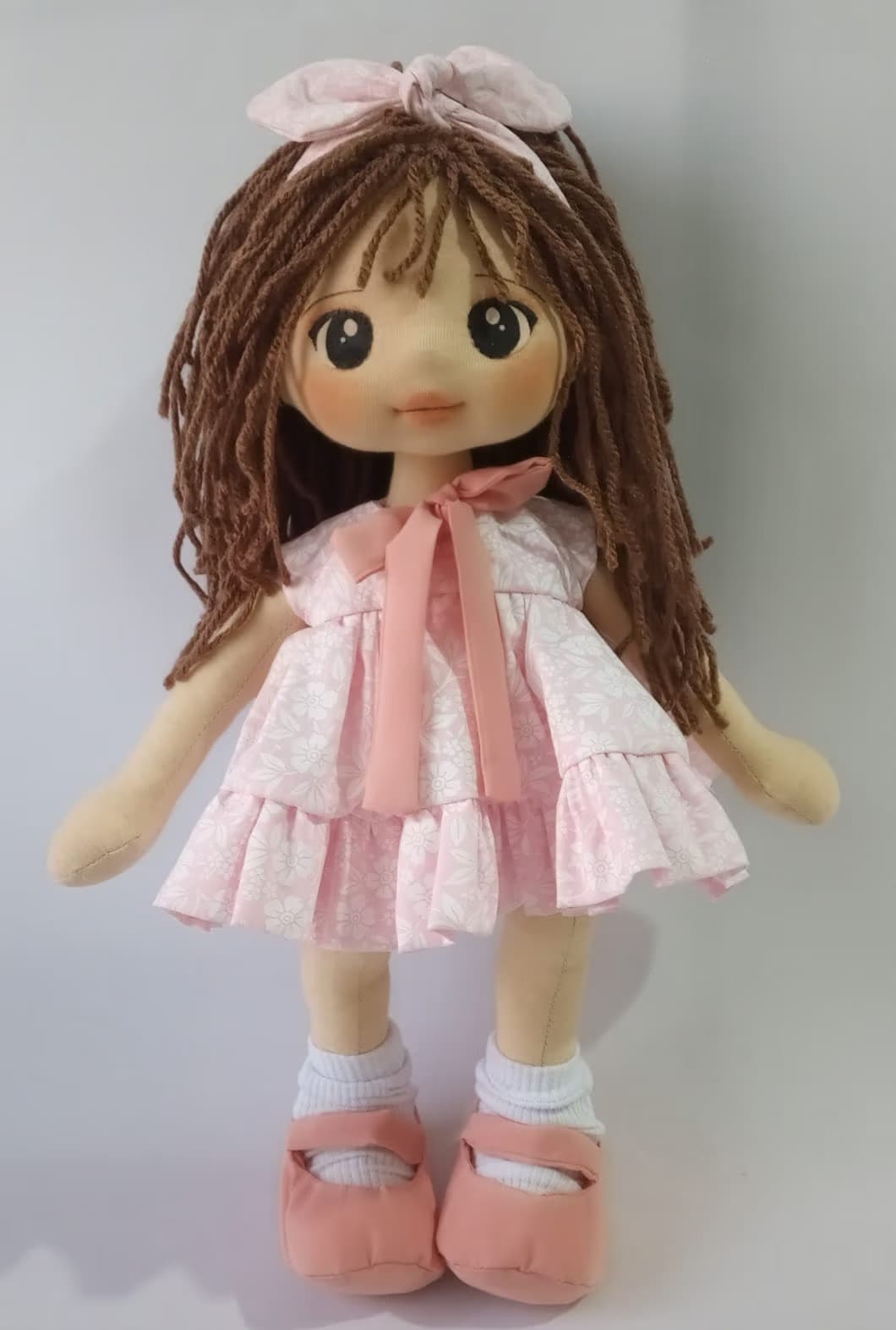 Boneca de pano morena com vestido rosa claro, sapatos rosa escuro e cabelo castanho