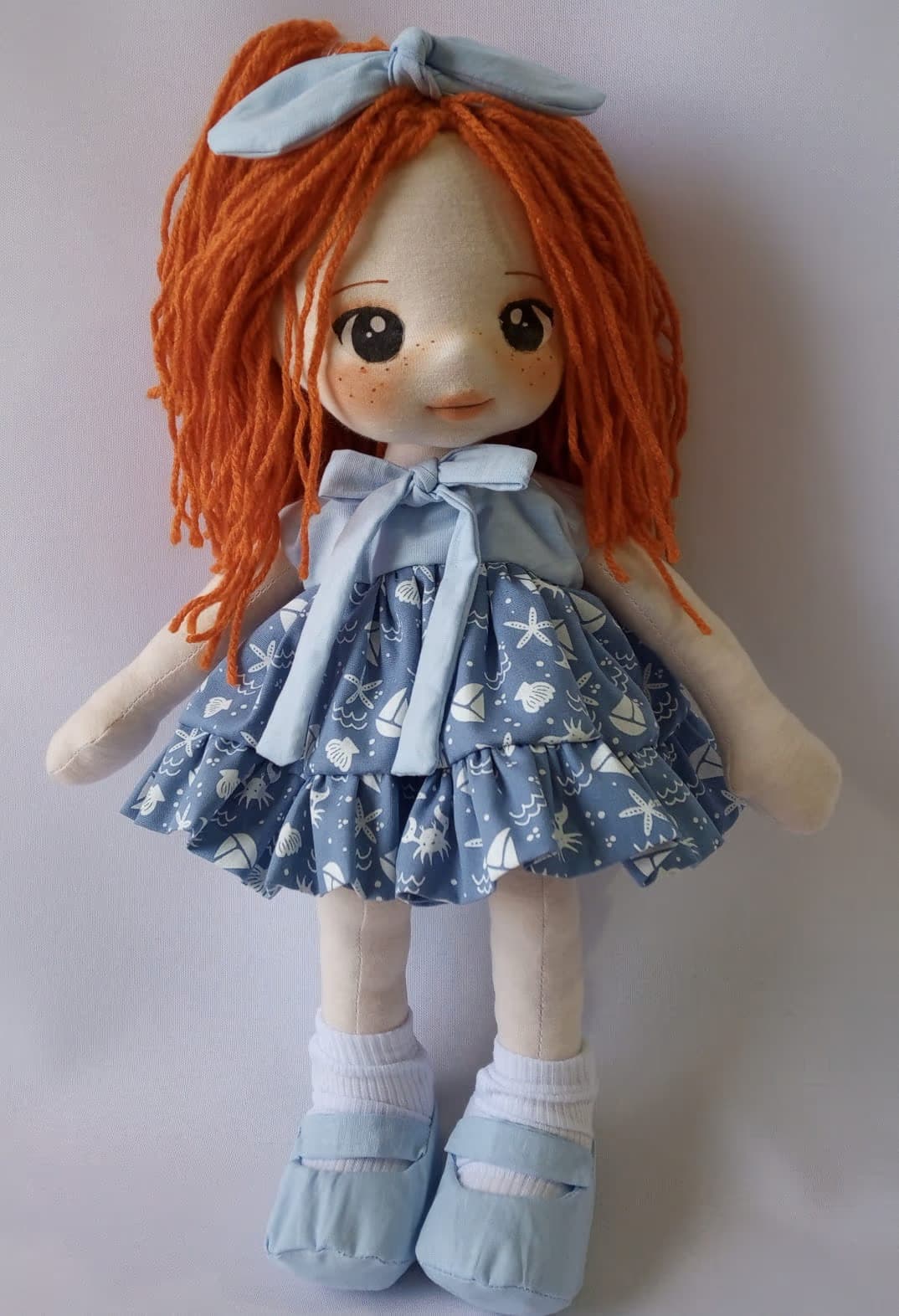 Boneca de pano ruiva com vestido azul marinho, sapato azul claro e laço azul claro