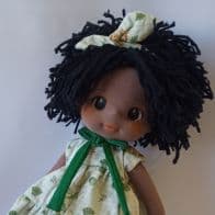 Selfe de boneca de pano negra com vestido verde e cabelo preto curto