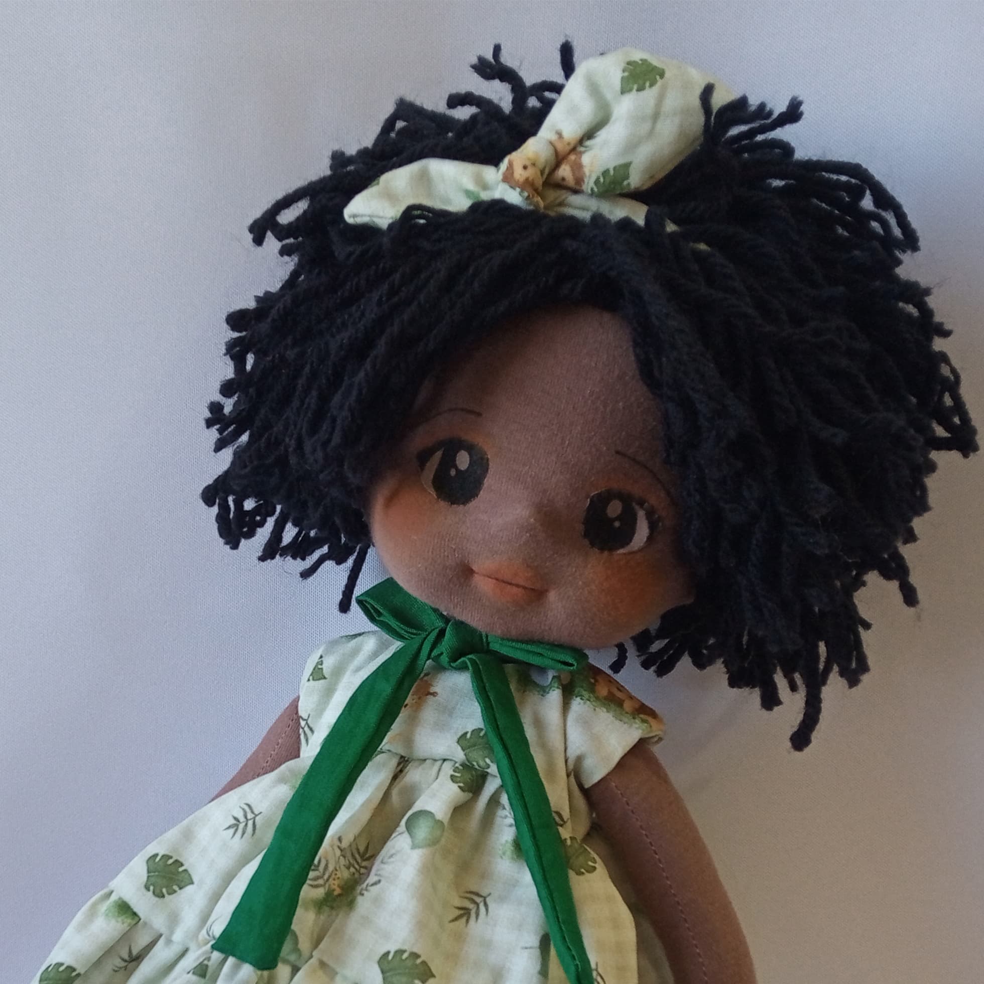 Selfe de boneca de pano negra com vestido verde e cabelo preto curto